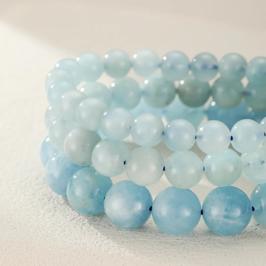 Trois bracelets en perles d'aigue-marine bleues pâles, disposés en dégradé sur une surface texturée blanche.