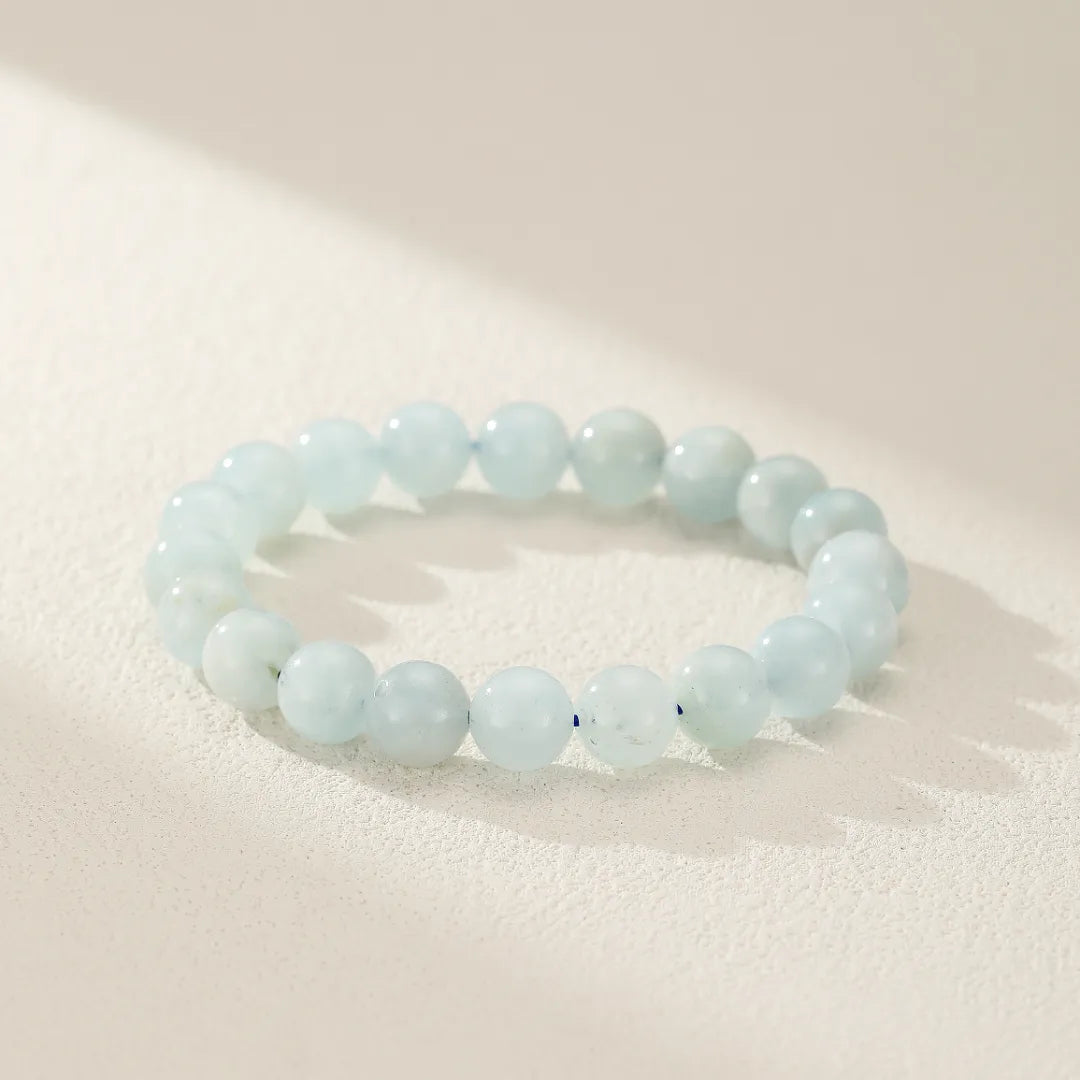 Bracelet "Douceur Calmante" en pierres d'aigue-marine naturelles, perles polies sur fond texturé clair avec jeu d'ombres.