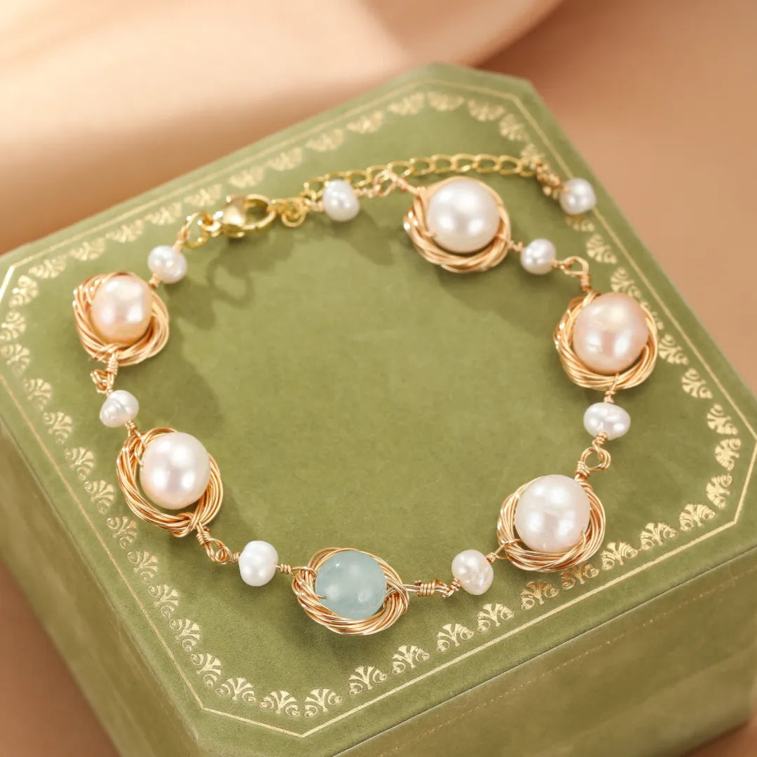Bracelet en or avec des perles blanches et roses et une pierre d'aigue-marine bleue, monté sur un fil torsadé et une chaîne fine.