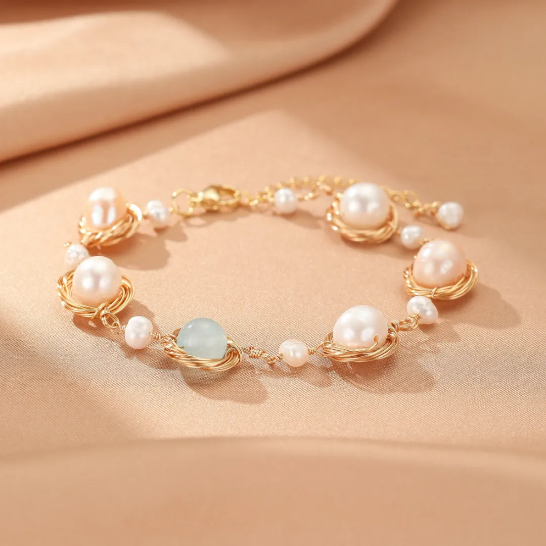 Bracelet "Mer Douce" en or avec des perles roses et blanches et des pierres d'aigue-marine disposées en nids, sur fond satiné beige.