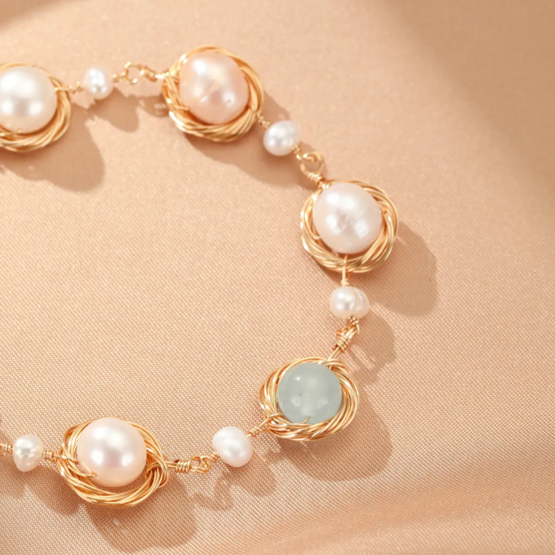 Bracelet fait à la main avec des perles d'eau douce roses et blanches, une pierre d'aigue-marine bleue pâle et du fil d'or torsadé sur un fond de soie beige.