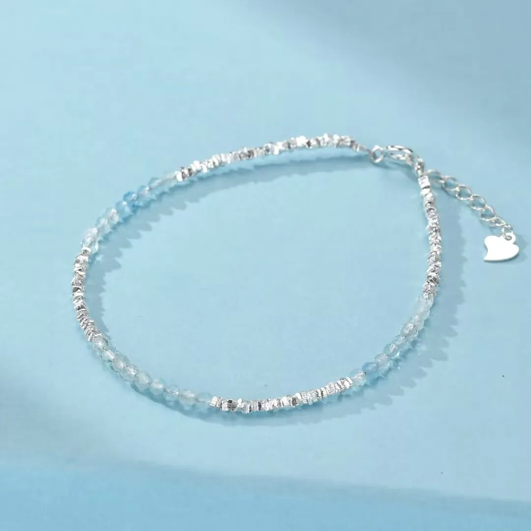 Bracelet "Murmure Douce" en argent avec de petites perles d'aigue-marine facettées et des éléments argentés texturés, doté d'une chaîne d'extension avec un fermoir en forme de cœur.