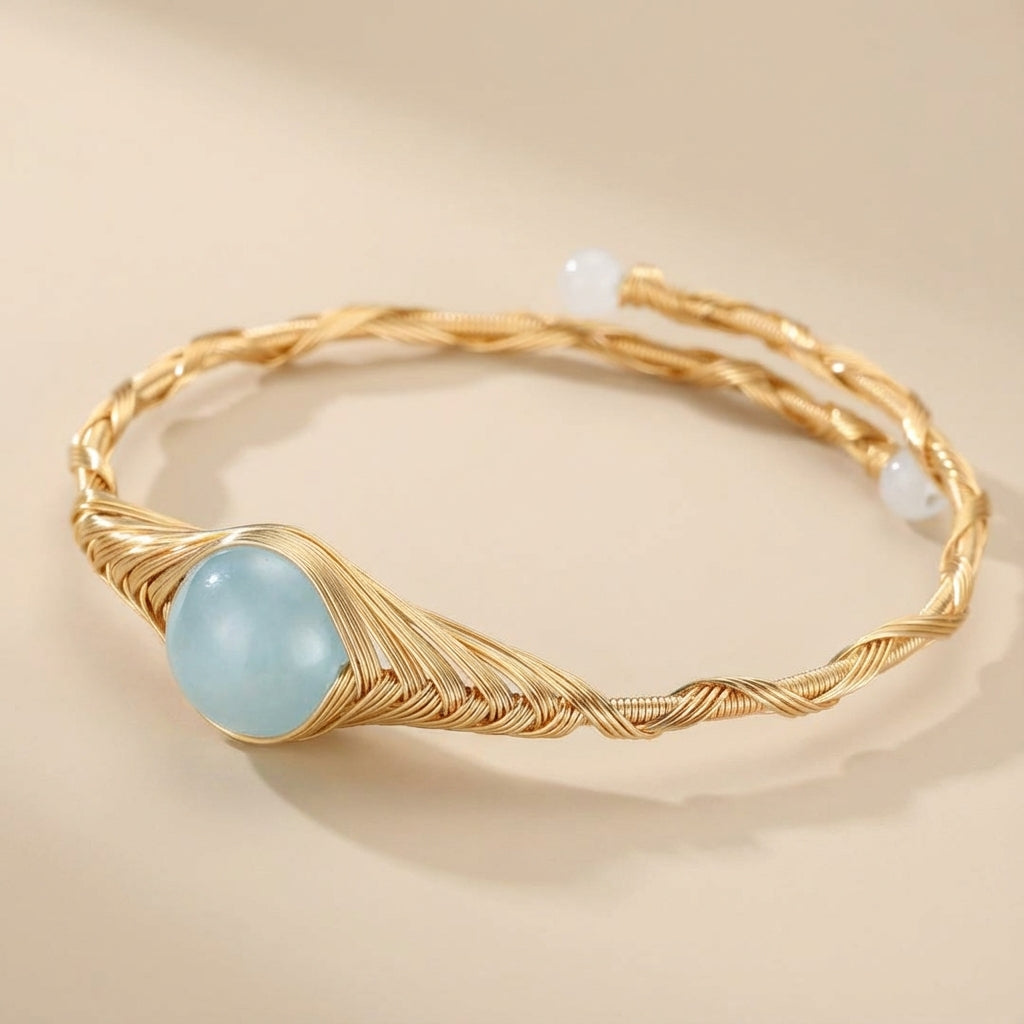 Bracelet en plaqué or 14K avec une pierre d'aigue-marine bleue et des détails torsadés, orné de petites perles blanches aux extrémités.