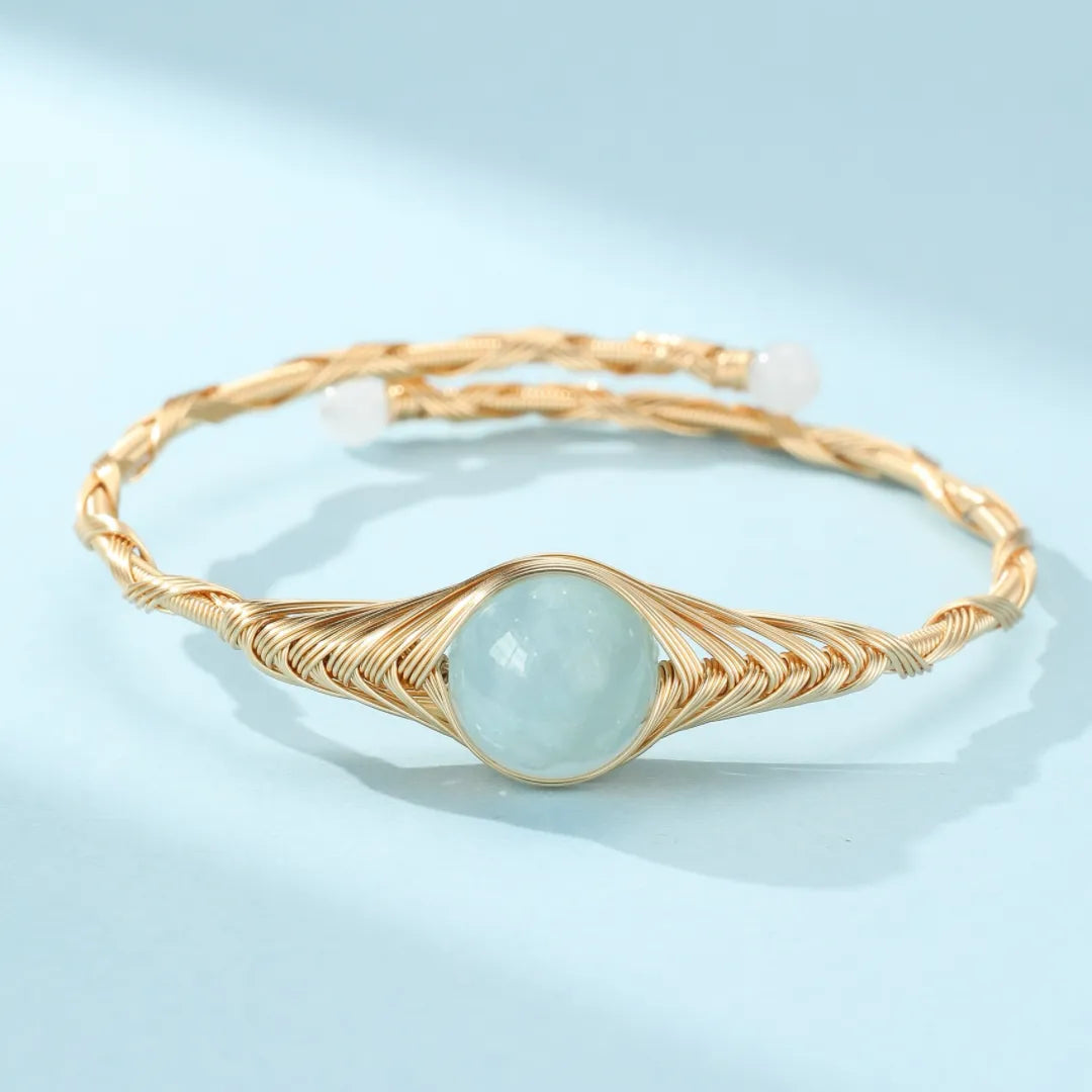 Bracelet jonc torsadé doré à l'or 14 carats avec une pierre d'aigue-marine bleue claire au centre.