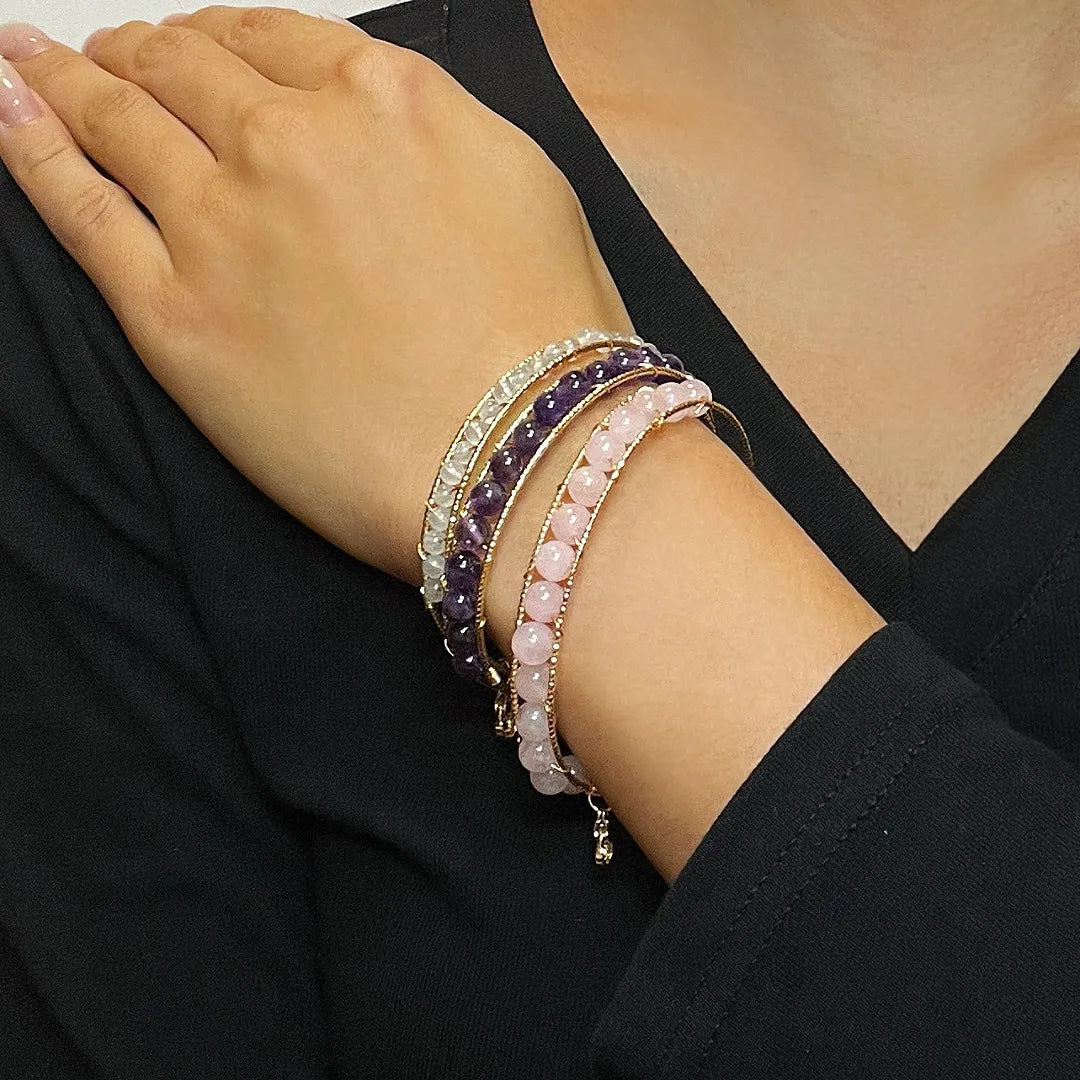Trois bracelets fins ornés de perles d'améthyste, de quartz rose et d'aigue-marine, portés sur un avant-bras.