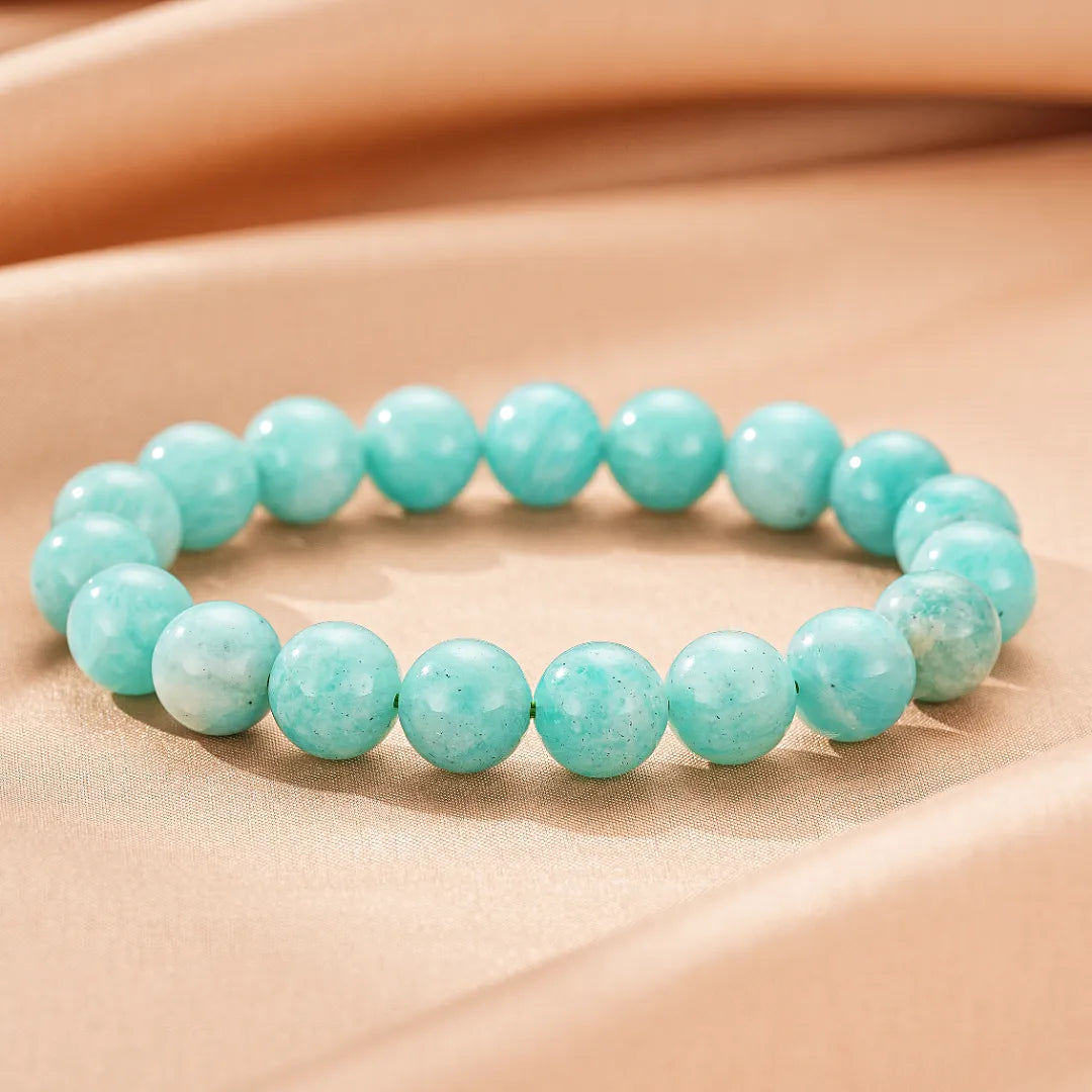 Bracelet fait de perles d'amazonite bleues claires, sur un fond de tissu beige satiné.