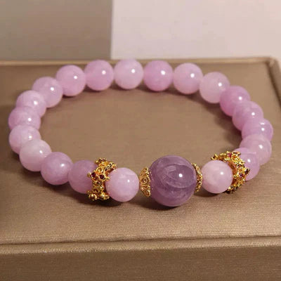 Bracelet élastique fait de perles rondes en améthyste et en quartz rose, avec des perles dorées ornées de motifs complexes entre les pierres.