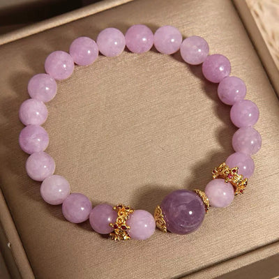 Bracelet élastique en perles d'améthyste lavande, rehaussé d'une perle centrale plus foncée et de séparateurs dorés ornés de petites pierres rouges.