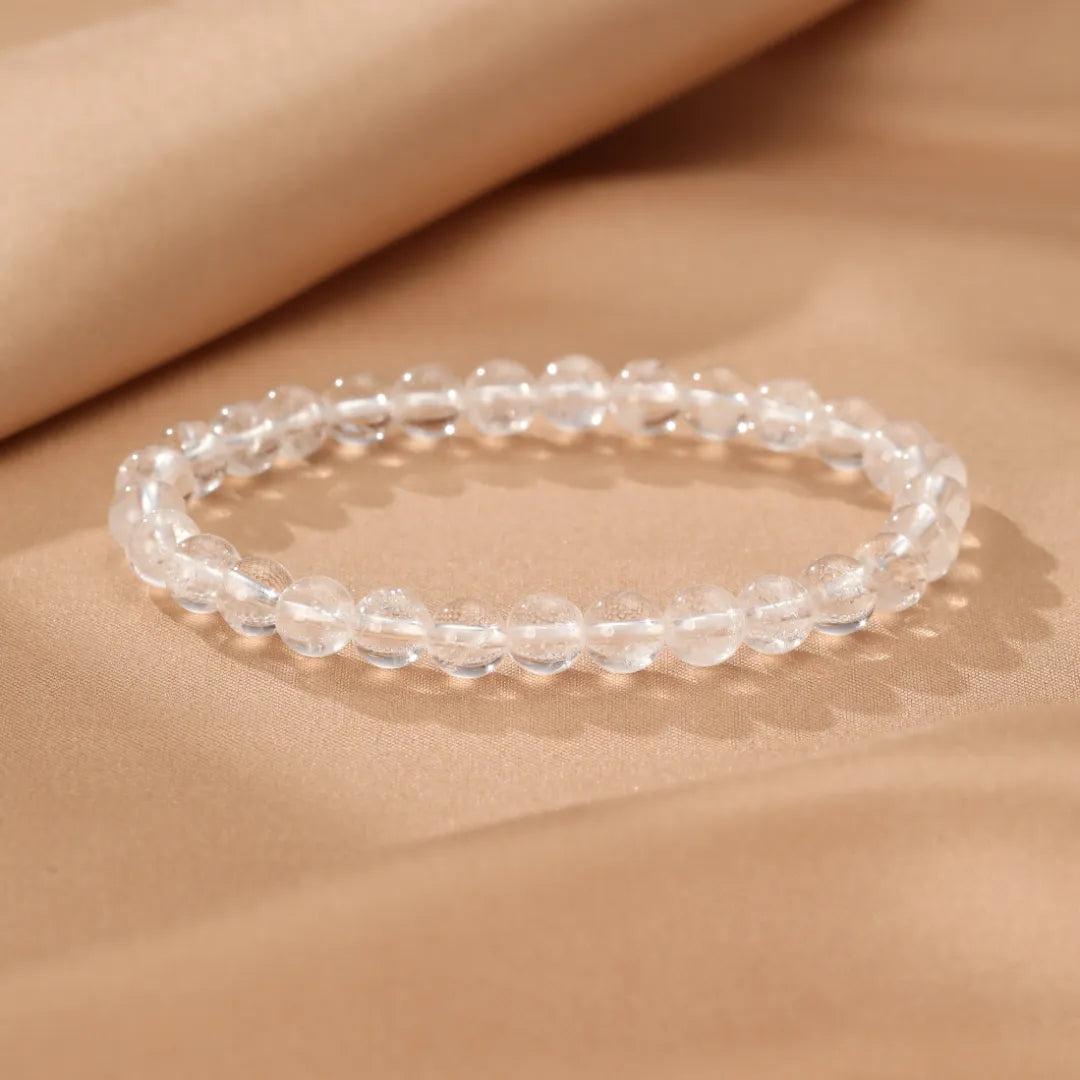 Bracelet en cristal de roche "Clarté Pure" avec des perles transparentes et facettées sur un fond beige satiné.