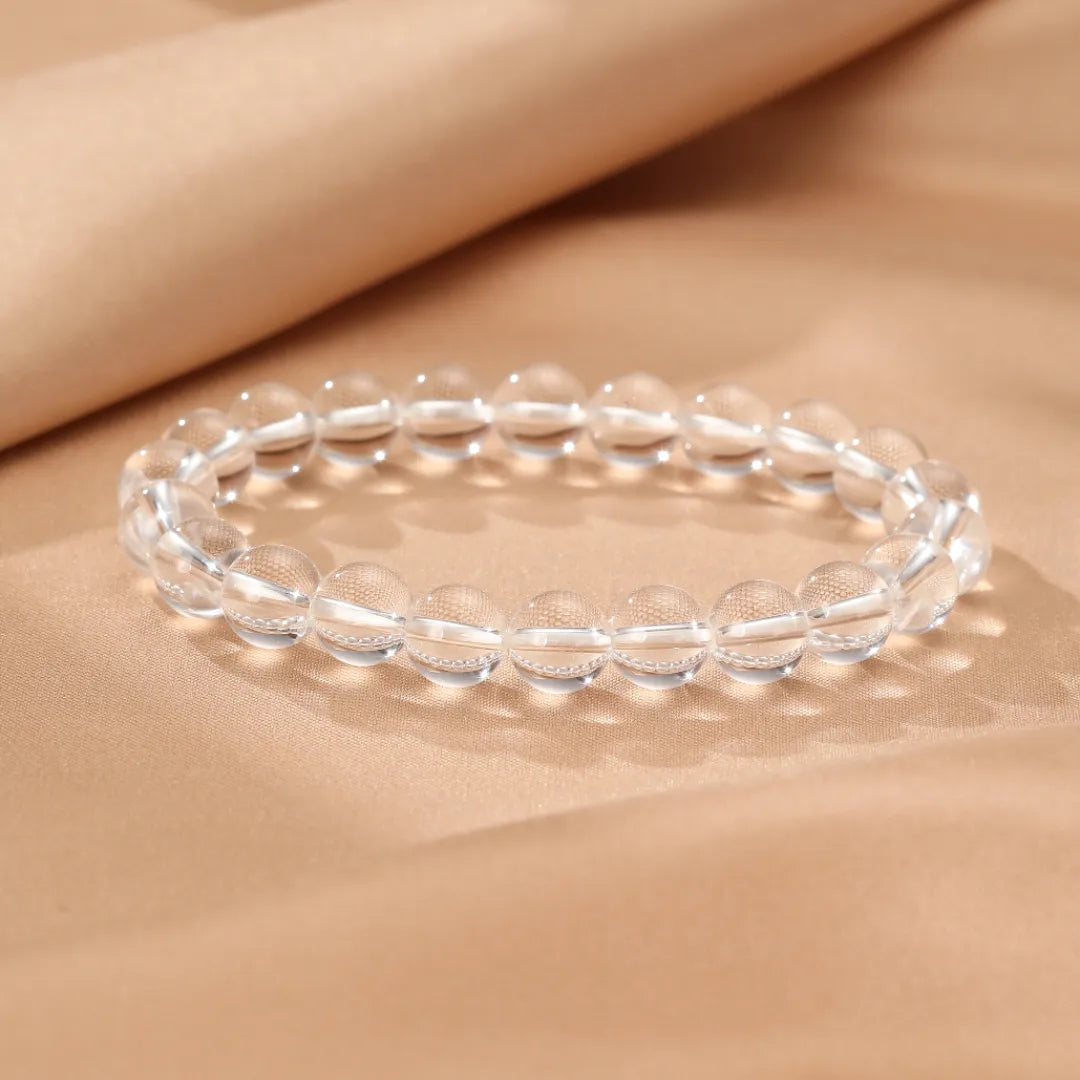 Bracelet en cristal de roche "Clarté Pure" composé de perles transparentes sur un fond beige satiné.