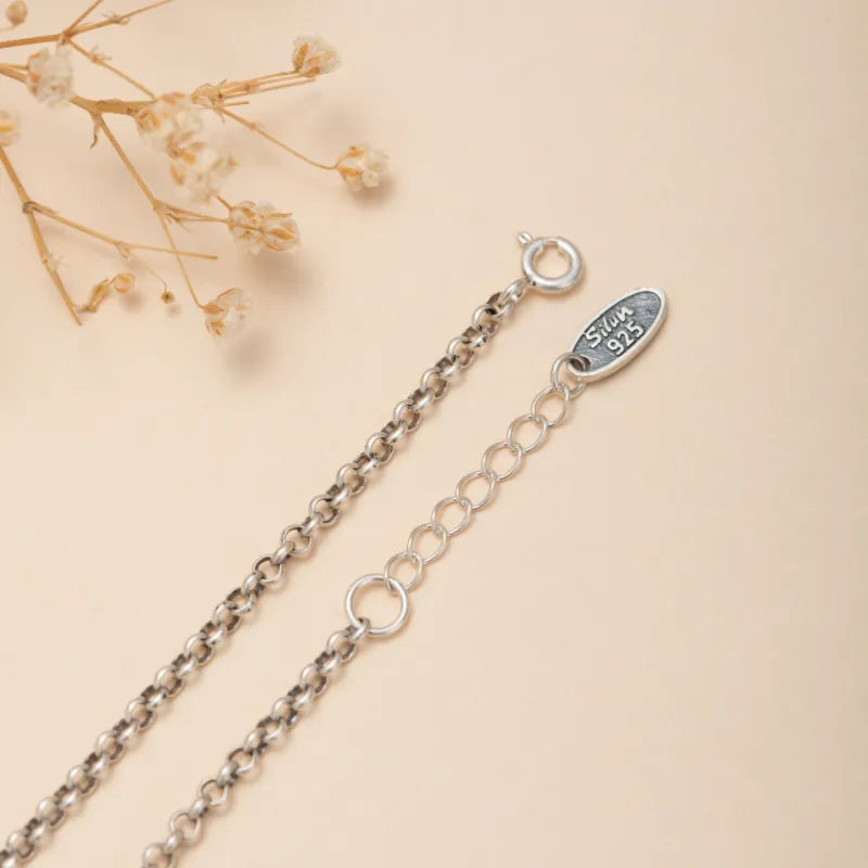 Gros plan sur la chaîne et le fermoir d'un bracelet de cheville en argent 925, avec une gravure "Silver 925" sur le pendentif ovale.
