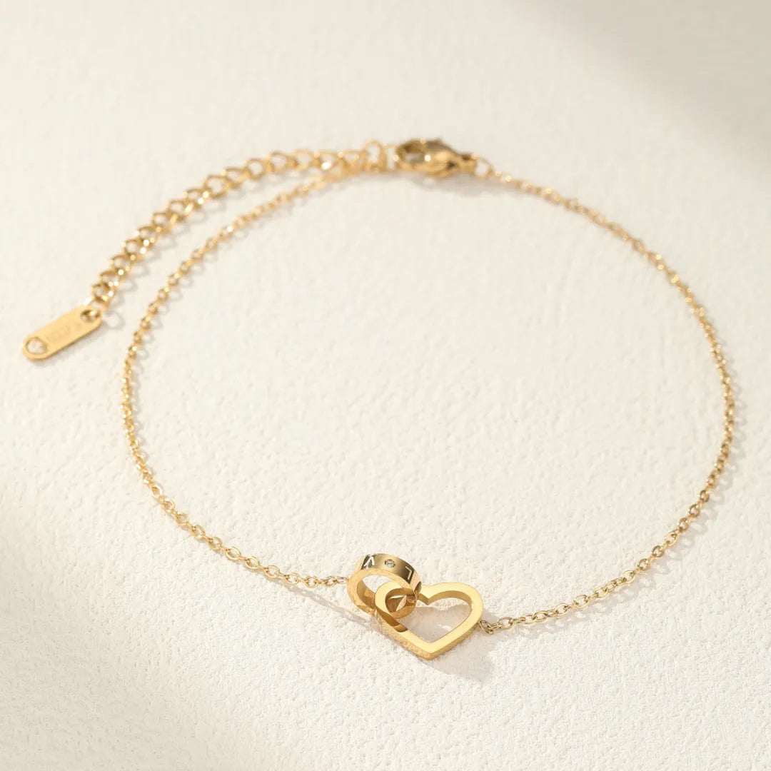 Bracelet de cheville en or fin avec un pendentif en forme de cœur entrelacé avec deux anneaux gravés de chiffres romains.