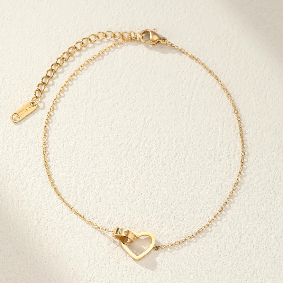 Bracelet de cheville doré avec un pendentif en forme de cœur stylisé, orné de deux anneaux entrelacés.