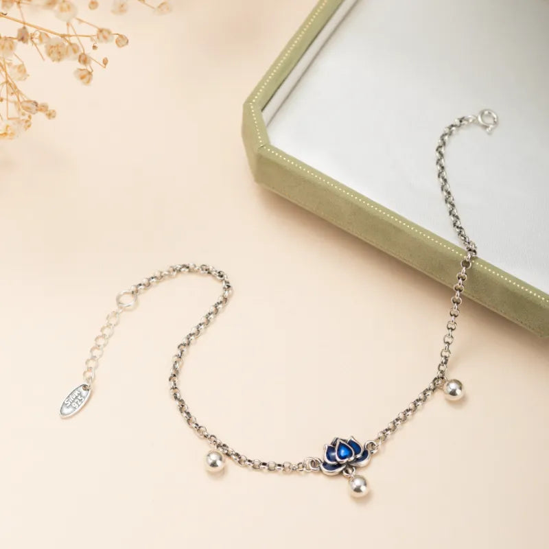 Bracelet de cheville en argent avec un pendentif en forme de lotus bleu et trois petites perles argentées. La chaîne est fine et ornée de petites boules argentées.