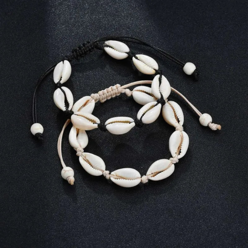 Deux bracelets de cheville faits de coquillages blancs naturels montés sur des cordons noirs et beiges, avec des fermetures ajustables à billes.