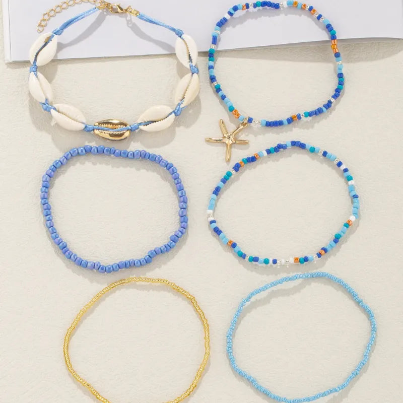 Ensemble de 5 bracelets de cheville, dont un orné de coquillages et d'une perle dorée, et un autre avec une étoile de mer dorée, le tout dans des tons bleus et dorés.