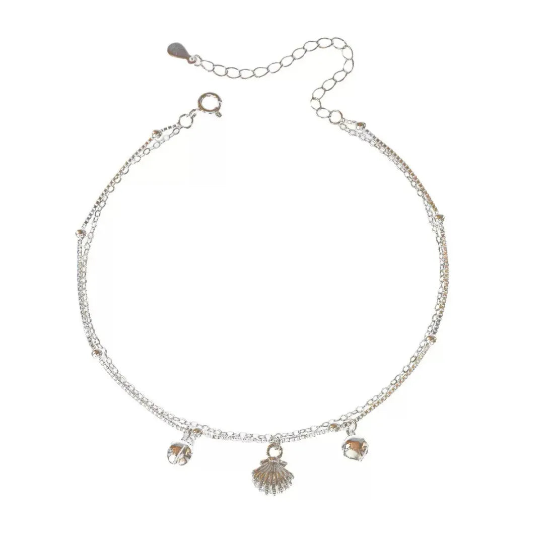 Bracelet de cheville double chaîne argenté avec pendentif coquillage central et deux perles rondes de chaque côté.