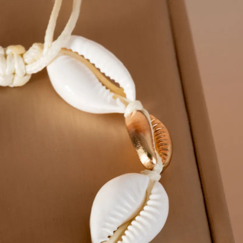 Bracelet de cheville "Protection Maritime" avec des cauris blancs et une perle dorée sur un cordon blanc.