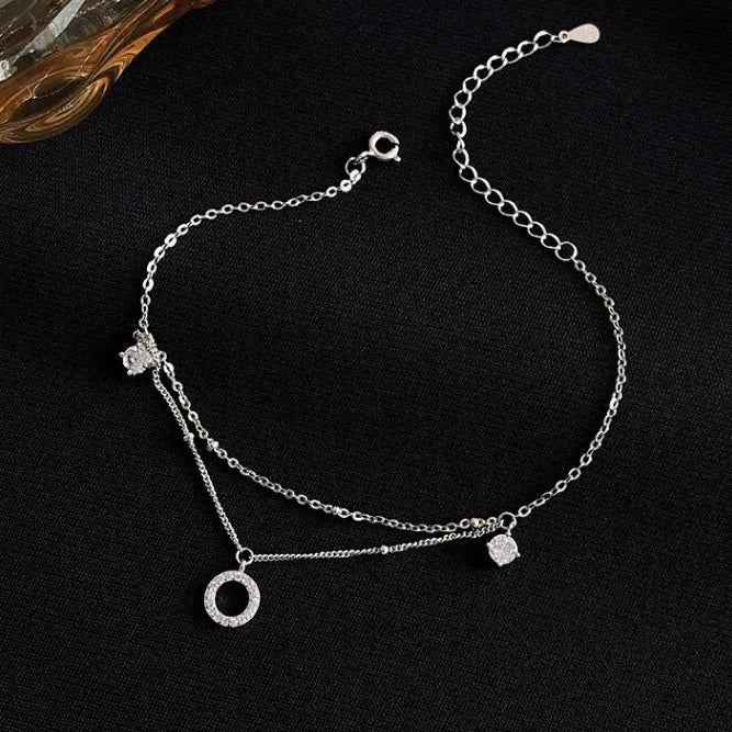 Bracelet de cheville double chaîne en argent 925 orné d'un pendentif rond pavé de zirconium et d'une petite pierre cubique.