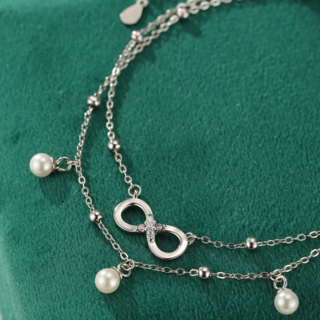 Bracelet de cheville double chaîne en argent 925 avec un pendentif infini serti de strass et des perles nacrées.