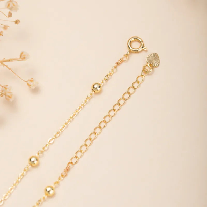 Bracelet de cheville en argent doré or avec une chaîne fine ornée de petites perles dorées et une breloque en forme de cœur texturé.