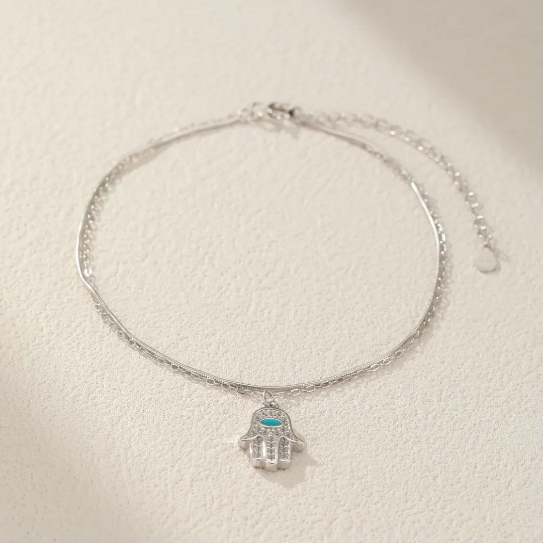 Bracelet de cheville en argent 925 avec pendentif Main de Fatma ornée de petites pierres bleues et blanches.