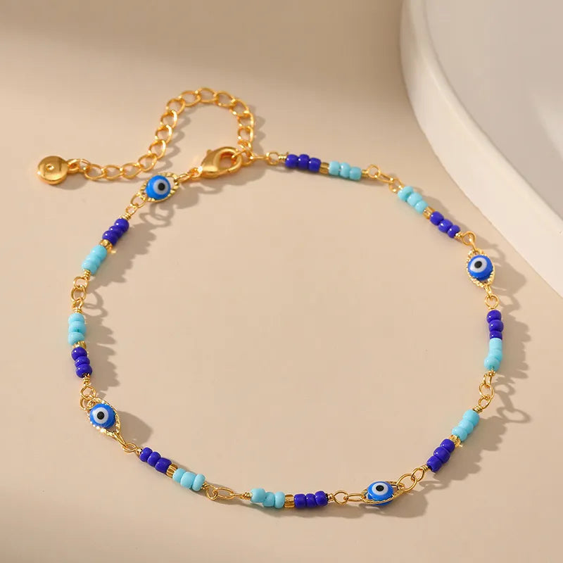 Bracelet de cheville doré avec des perles bleues et turquoises alternant avec des breloques œil bleu protecteur.