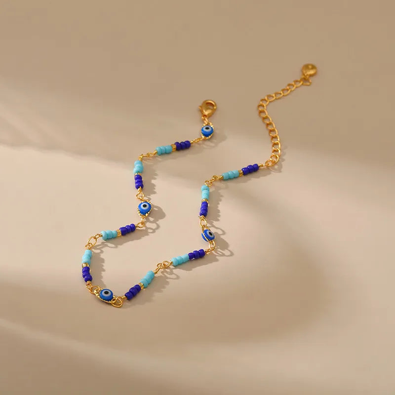 Bracelet de cheville doré or avec perles bleues et turquoises et breloques œil bleu protecteur.