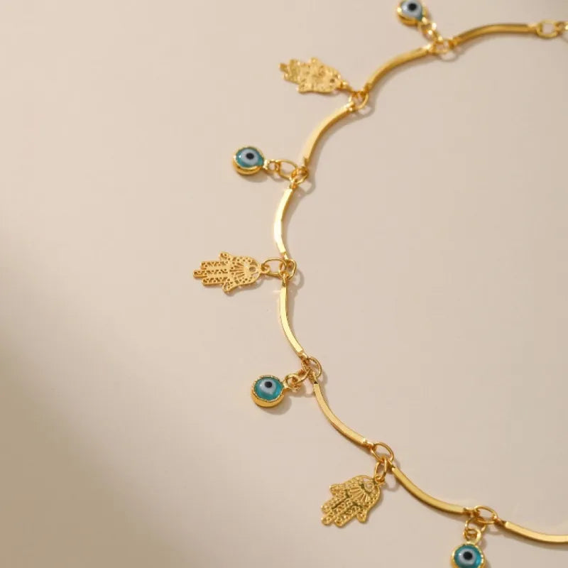 Bracelet de cheville doré or orné de breloques "Mauvais Œil" bleues et de mains de Fatma ("Khamsa") ajourées, symboles de protection.