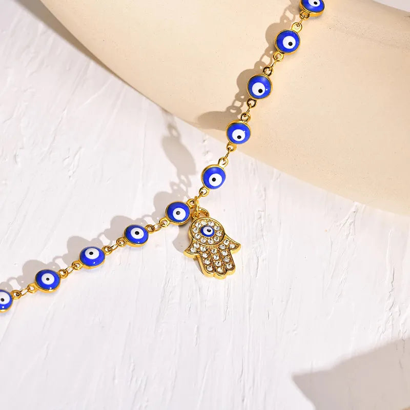 Bracelet de cheville doré orné de perles œil bleu et d'un pendentif main de Fatma serti de strass.