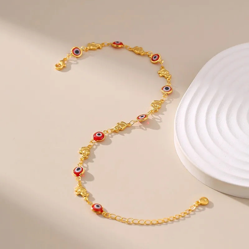 Bracelet de cheville doré à l'or orné de multiples breloques œil du mal rouge et bleu et d'éléphants dorés, avec une chaîne délicate et un fermoir réglable.