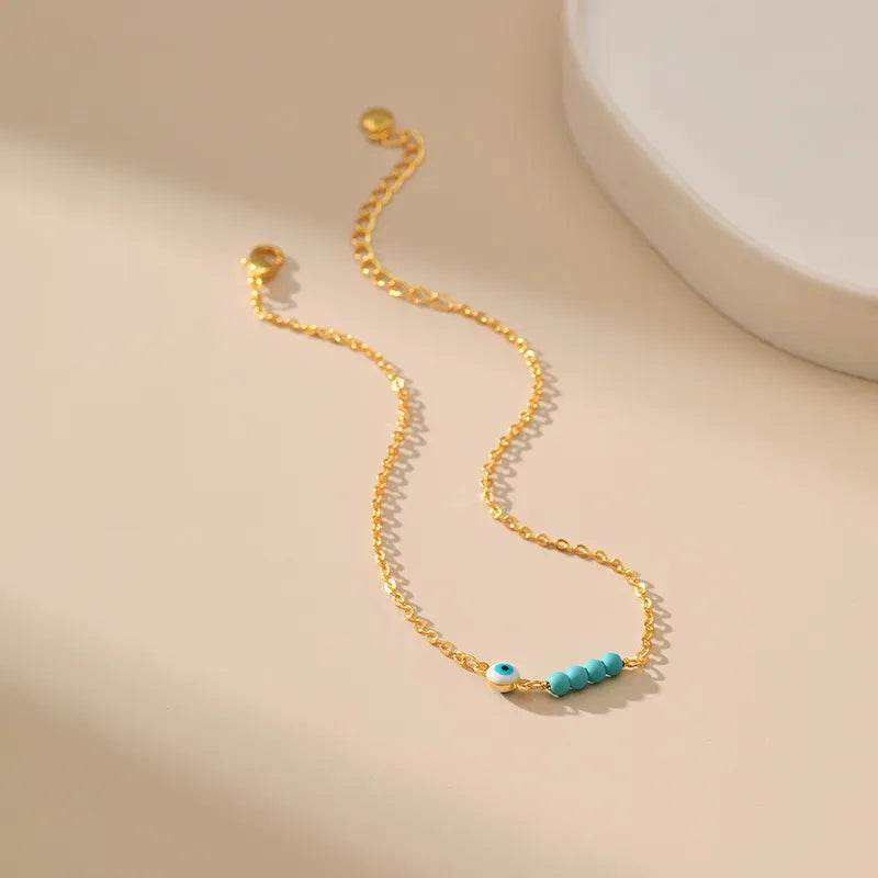 Bracelet de cheville doré fin avec une petite breloque œil bleu et trois perles turquoise alignées sur la chaîne.