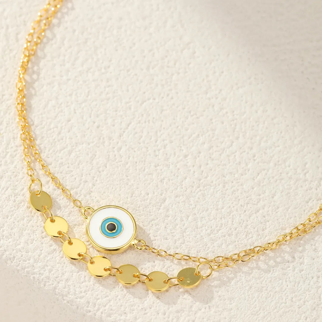 Bracelet de cheville "Regard Ancestral" en argent 925, avec une double chaîne ornée de petites rondelles dorées et un pendentif œil bleu et blanc.