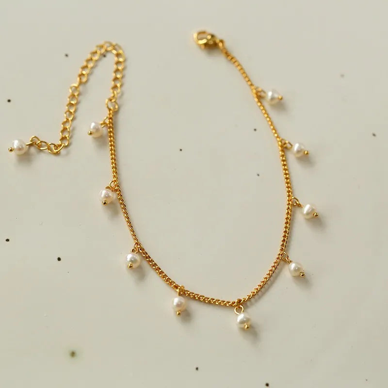 Bracelet de cheville doré à petites perles blanches suspendues à une chaîne délicate, fermoir mousqueton.