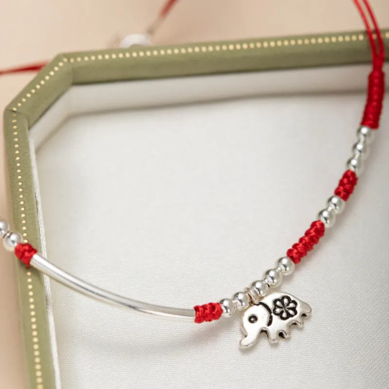 Bracelet de cheville "Petite Éléphant" en argent avec perles argentées et fil rouge, orné d'un pendentif éléphant fleuri.