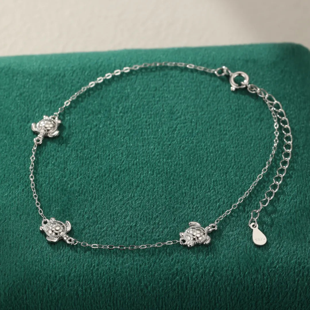 Bracelet de cheville en argent 925 avec quatre petites tortues incrustées de strass, fermoir mousqueton et chaînette d'extension.