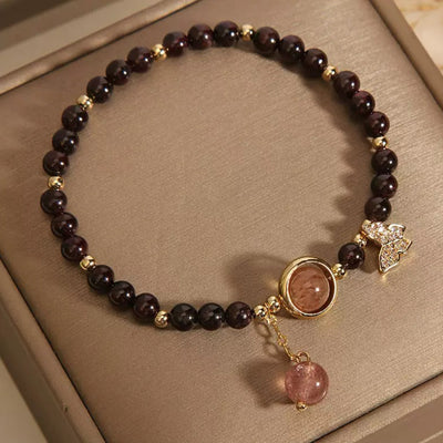 Bracelet en grenat et quartz fraise avec un pendentif papillon scintillant et une perle ronde rose suspendue, monté sur une chaîne dorée.