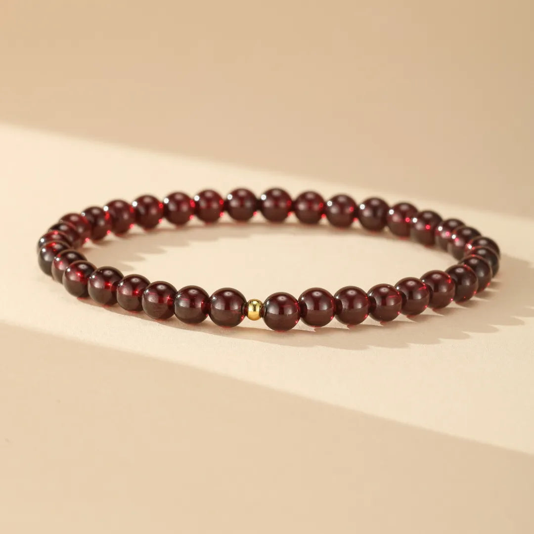 Bracelet fin "Passion" en grenats naturels et une perle dorée centrale, sur fond beige.