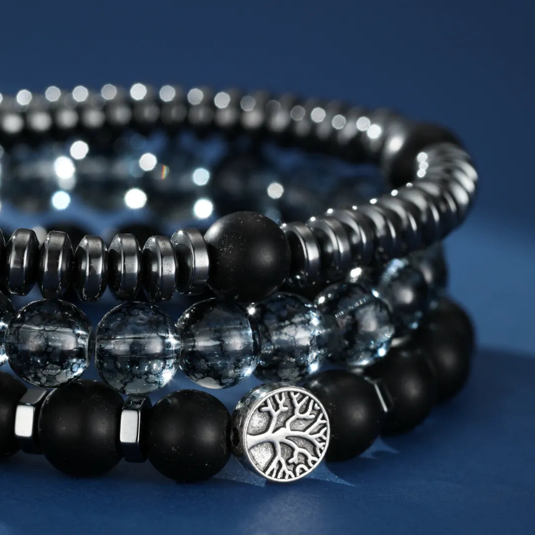 Trois bracelets empilables pour homme : un avec des perles d'hématite, un autre avec des perles d'obsidienne et des perles de cristal, le troisième avec des perles d'obsidienne et un fermoir arbre de vie en argent.
