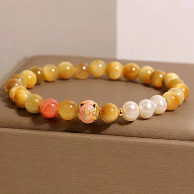 Bracelet élastique avec des perles œil de tigre dorées, une perle rose corail, une perle centrale sculptée rose avec des détails dorés et des perles de culture blanches.