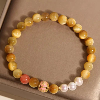 Bracelet élastique fait de perles d'œil de tigre dorées, de perles roses, de perles blanches et d'une perle décorative rose et dorée au centre.