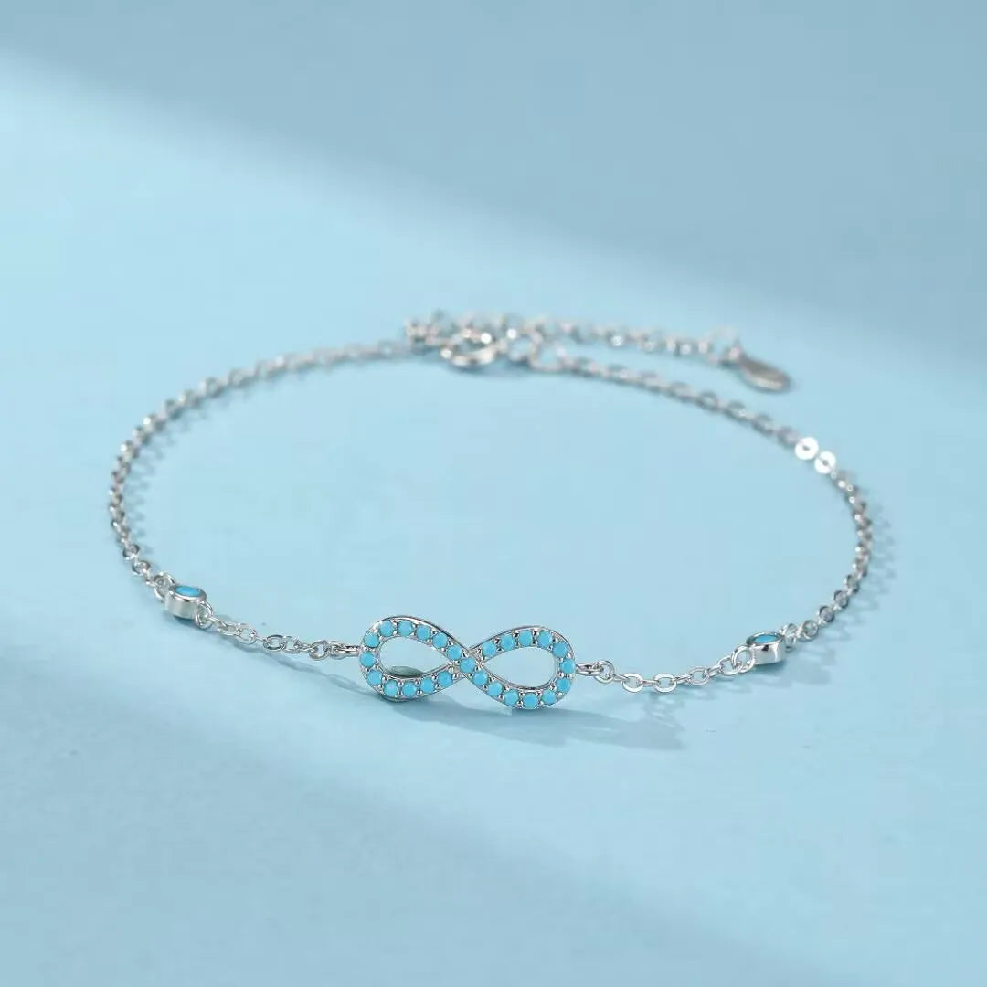 Bracelet infini argent 925 orné de turquoises bleues, le bijou "Souffle d'Infini" est présenté sur un fond bleu clair.