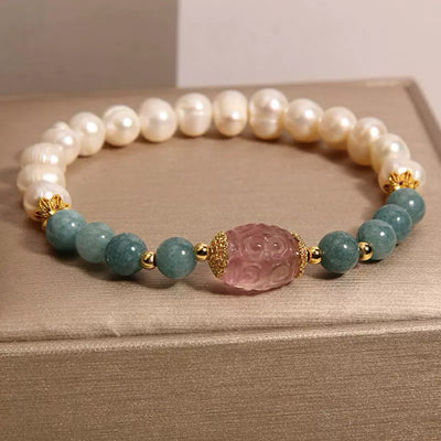 Bracelet élastique avec perles de jade blanc, perles d'eau douce nacrées et une pierre centrale sculptée rose, rehaussé d'éléments dorés.