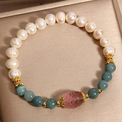 Bracelet élastique en perles de jade blanc, perles de fluorite bleu-vert et une pièce centrale sculptée en quartz rose, avec des accents dorés.