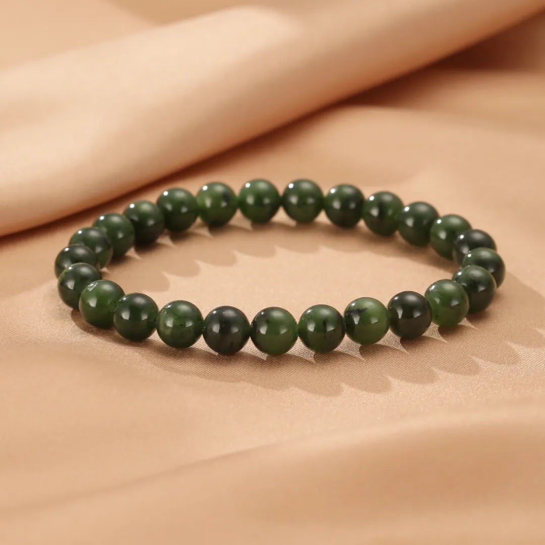 Bracelet "Sérénité Naturelle" fait de perles de jade vert foncé, posé sur un tissu beige satiné.