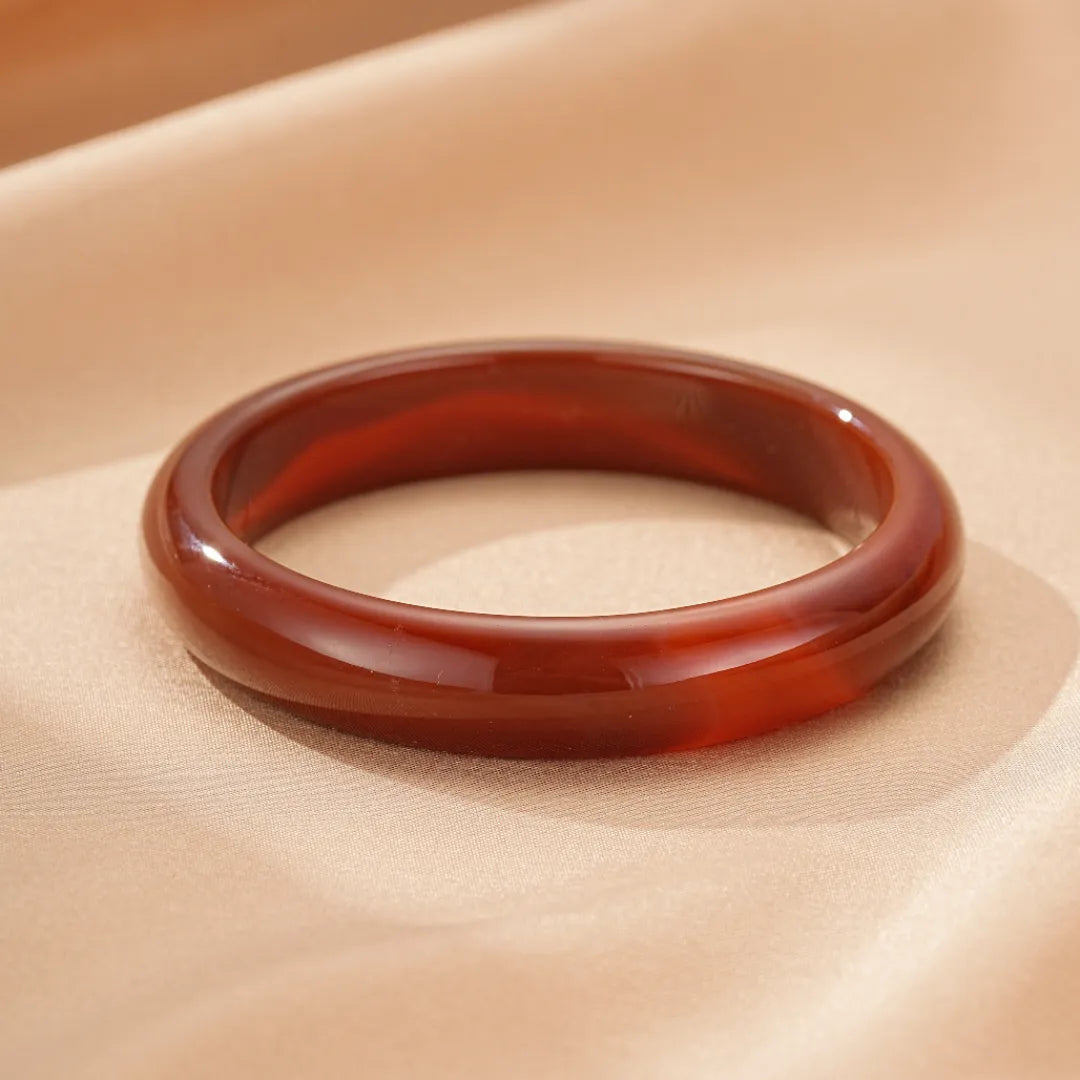 Bracelet jonc en agate rouge translucide, nommé "Force Audacieuse", sur un tissu beige.