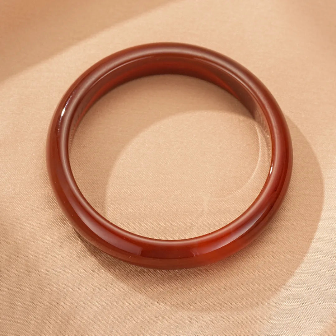 Bracelet jonc en agate rouge profond, style minimaliste, sur un fond beige satiné.