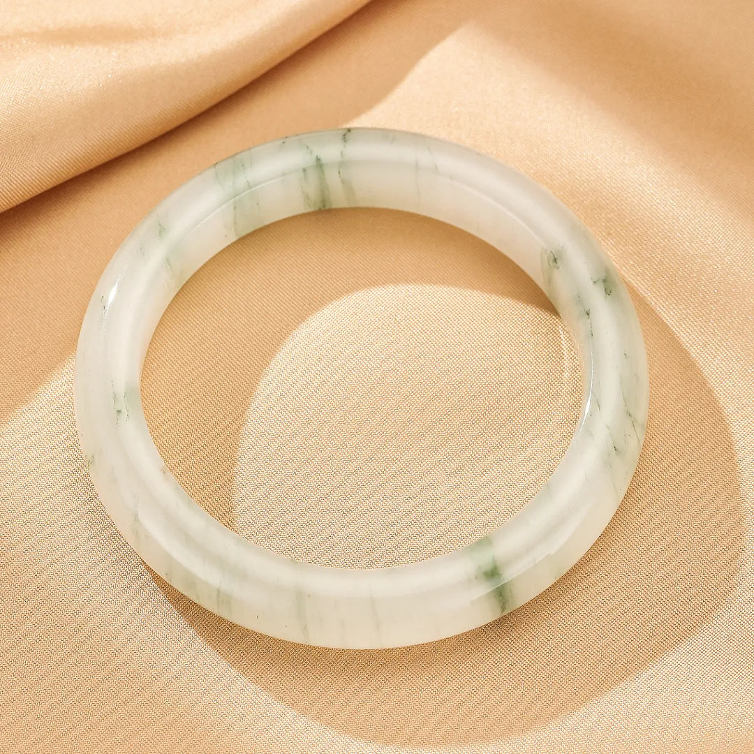 Bracelet jonc en calcédoine blanche et verte « Éclat de Nature » sur un fond satiné beige.
