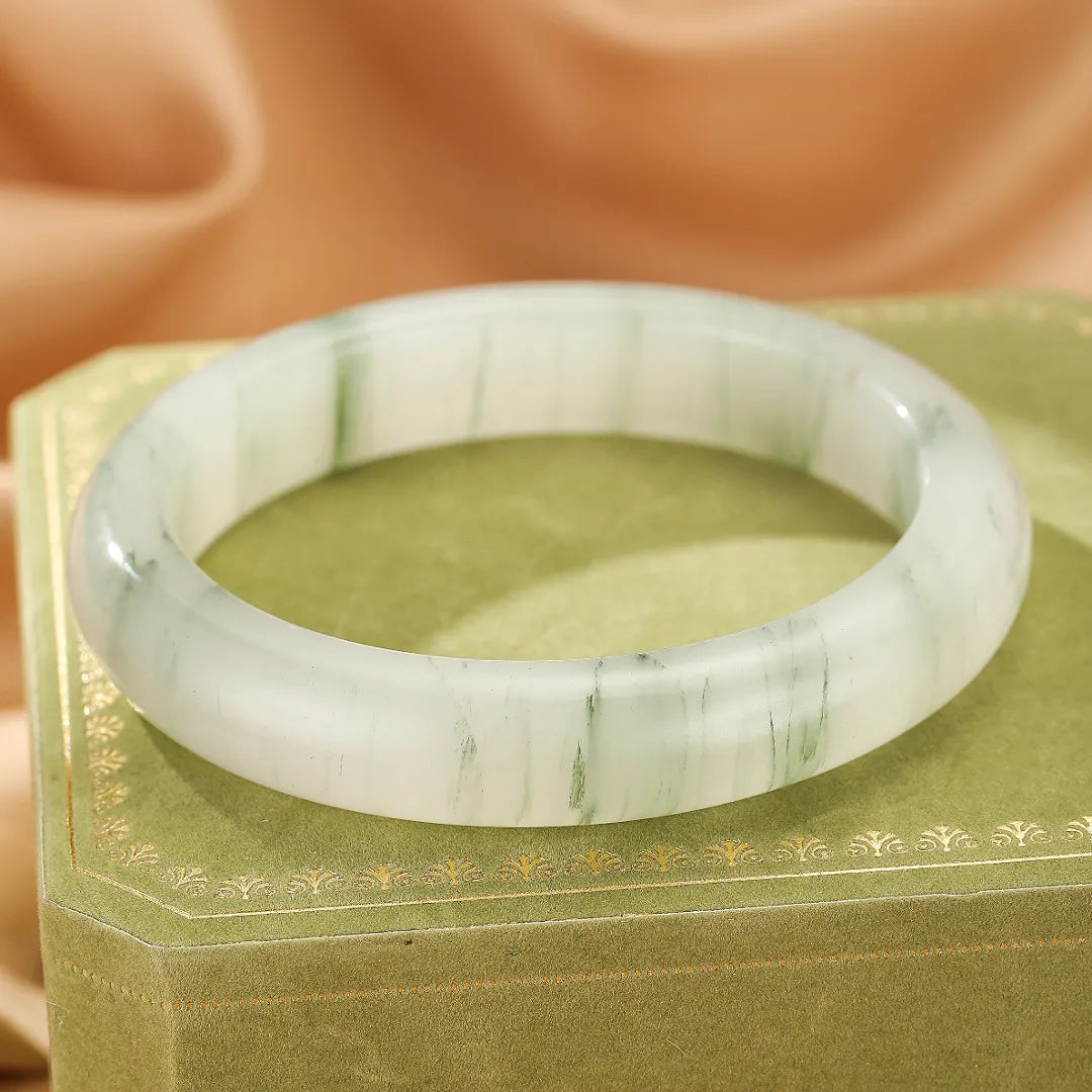 Bracelet jonc en calcédoine blanche et verte avec des marbrures naturelles, posé sur un écrin vert.