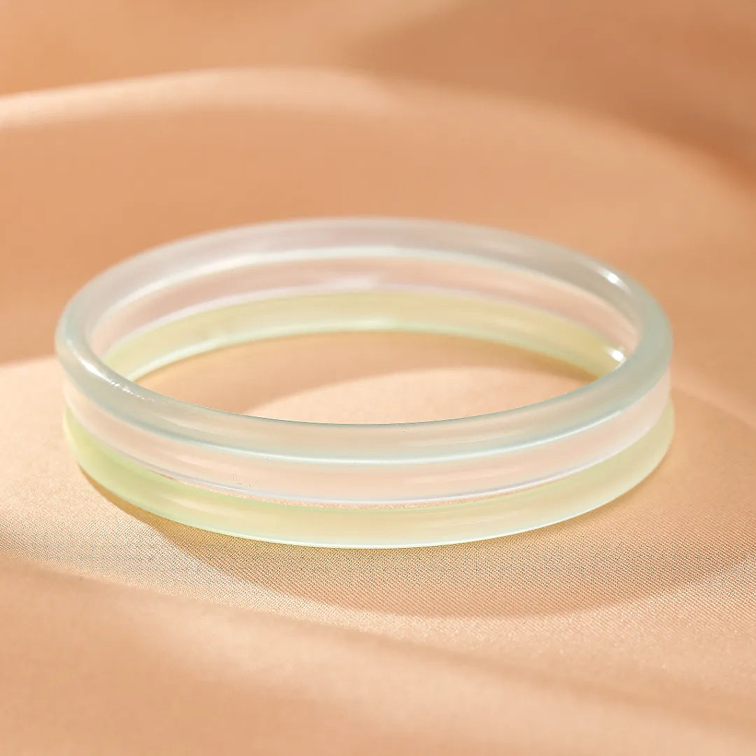 Bracelet jonc en calcédoine aux teintes douces d'eau et de menthe, posé sur un tissu satiné couleur pêche.